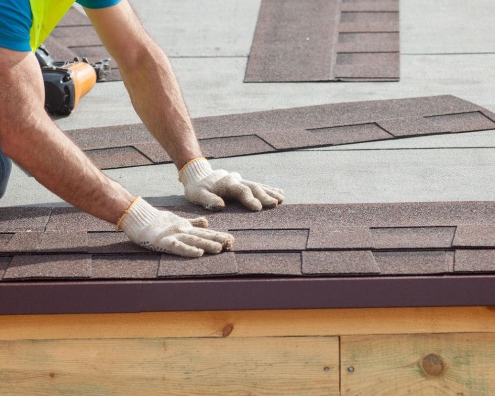 A person with gloves on working on the roof of a house.