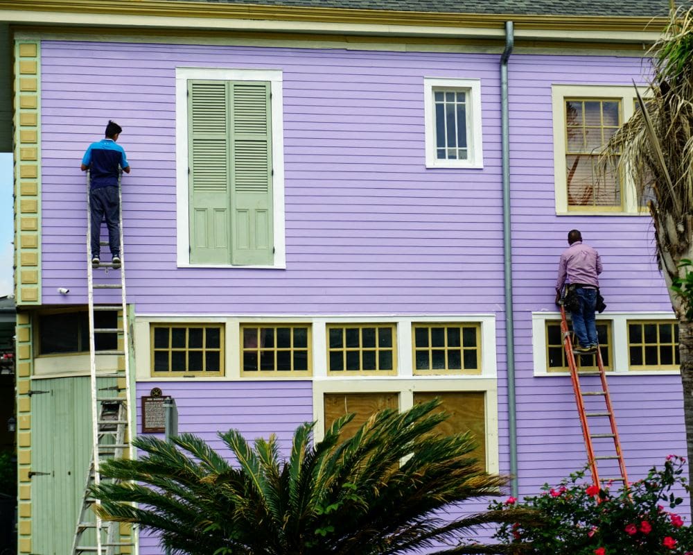 Two men on a ladder painting the outside of a house.